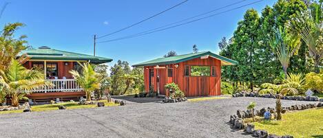 A two-story building with a green roof, surrounded by tropical vegetation and a gravel driveway.