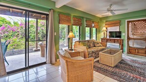 A living room with a sofa, a wicker chair, a glass-top coffee table, and a TV stand.
