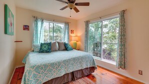 A bedroom with a bed, a ceiling fan, two windows with curtains, and a nightstand with a lamp. - Breezy Kailua-kona Bungalow w/ Lanai & Ocean View! (Kailua-Kona)