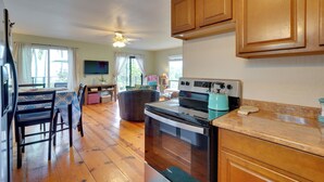 A kitchen with wooden cabinets, a stove, and a dining area with chairs and a table. - Breezy Kailua-kona Bungalow w/ Lanai & Ocean View! (Kailua-Kona)
