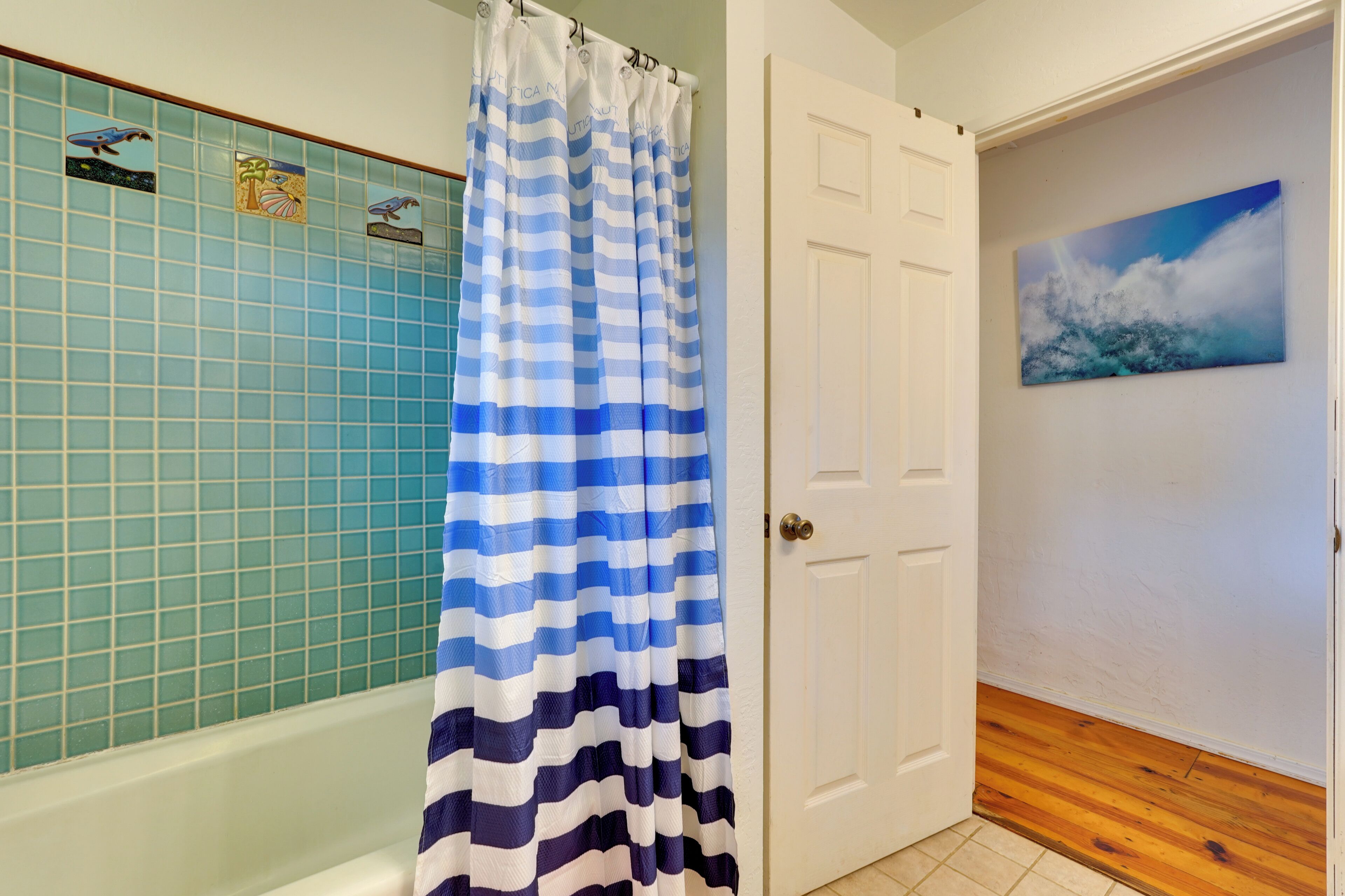 A bathroom with a blue and white striped shower curtain, a tiled wall with a bird pattern, and a wooden floor.