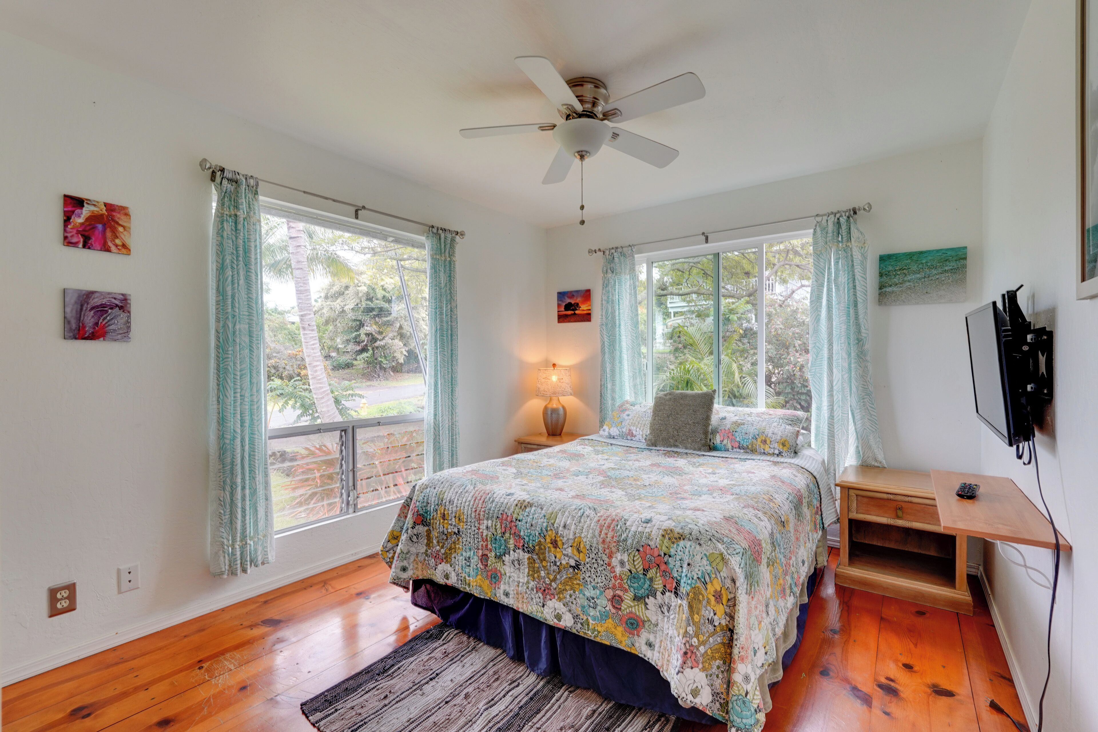 A bedroom with a bed, a ceiling fan, a nightstand, a lamp, a TV, and a window with curtains.
