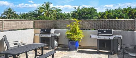 Une terrasse extérieure équipée de deux barbecues, d’une table et de chaises.