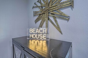 Kirkkaasta akryylistä valmistetussa jalustassa on kyltti, jossa lukee ”BEACH HOUSE”. Sen takana olevalla seinällä on tähtimäinen metallikoriste.