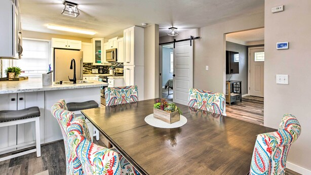 A modern kitchen with white cabinets, a central island, and a dining area with a wooden table and colorful patterned chairs. - Walk to Lake Pepin: Charming Retreat w/ Deck (Pepin)