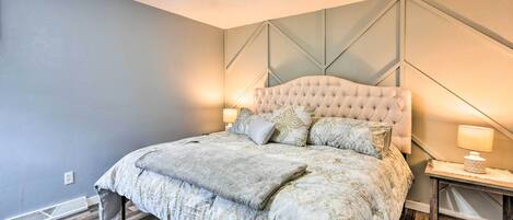 A bedroom with a tufted headboard, a bed with a patterned duvet, a wooden floor, and a ceiling fan.