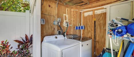 A laundry area with a white washer and dryer, wooden walls, and a ceiling light.