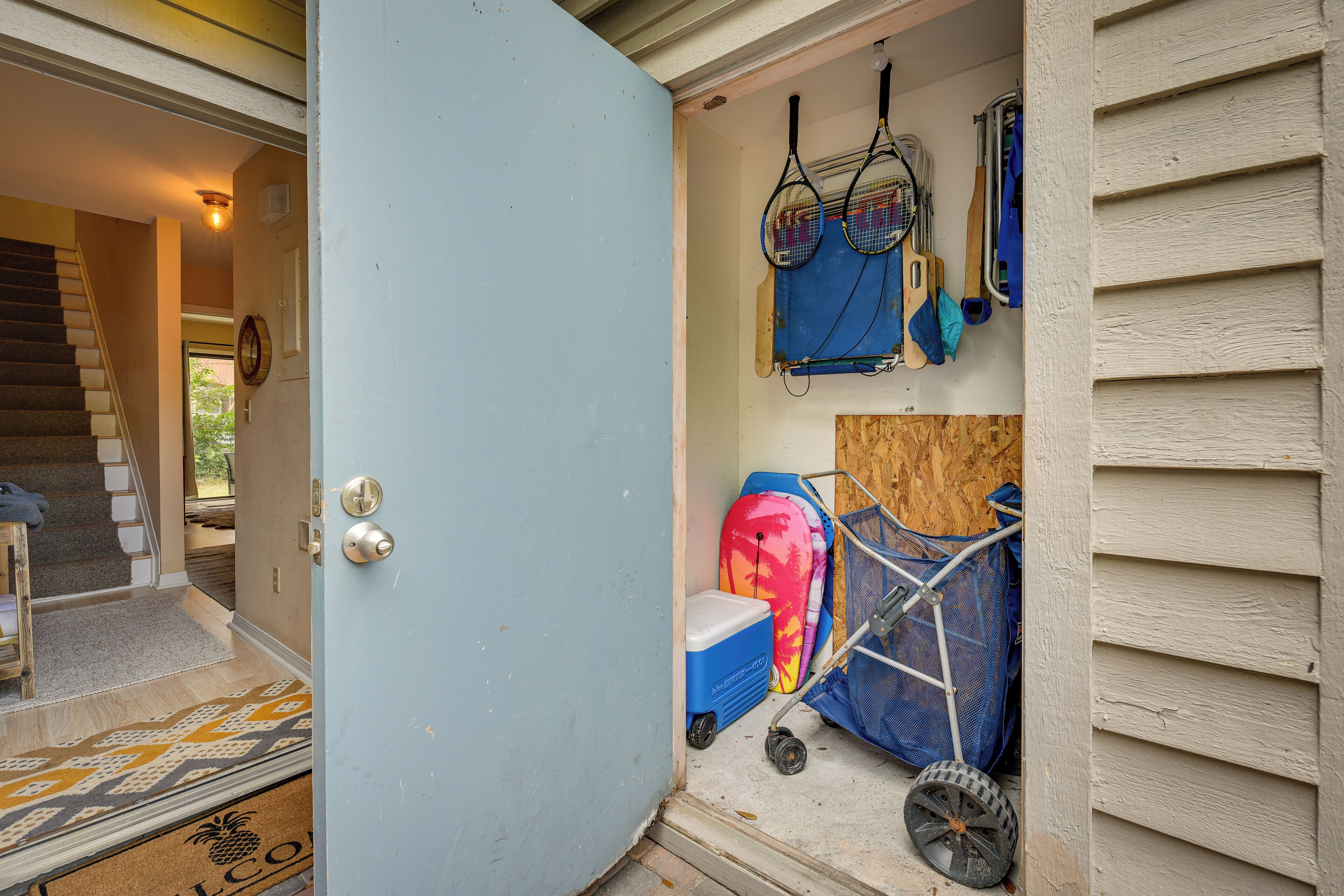 A door leading to a room with a wooden floor, a blue mat, and a welcome mat.