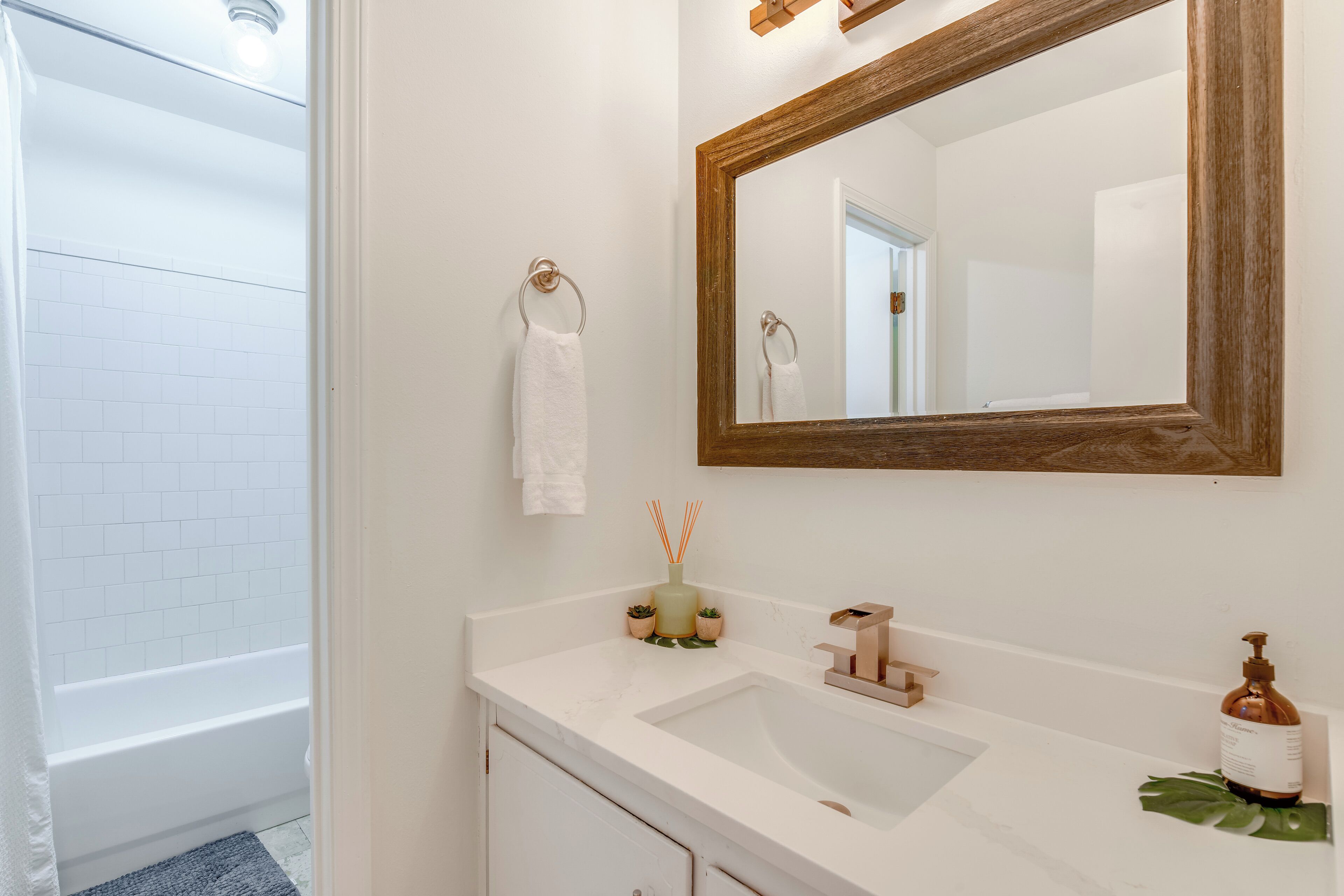 A bathroom with a white sink, a mirror with a wooden frame, a towel ring, and a small plant.