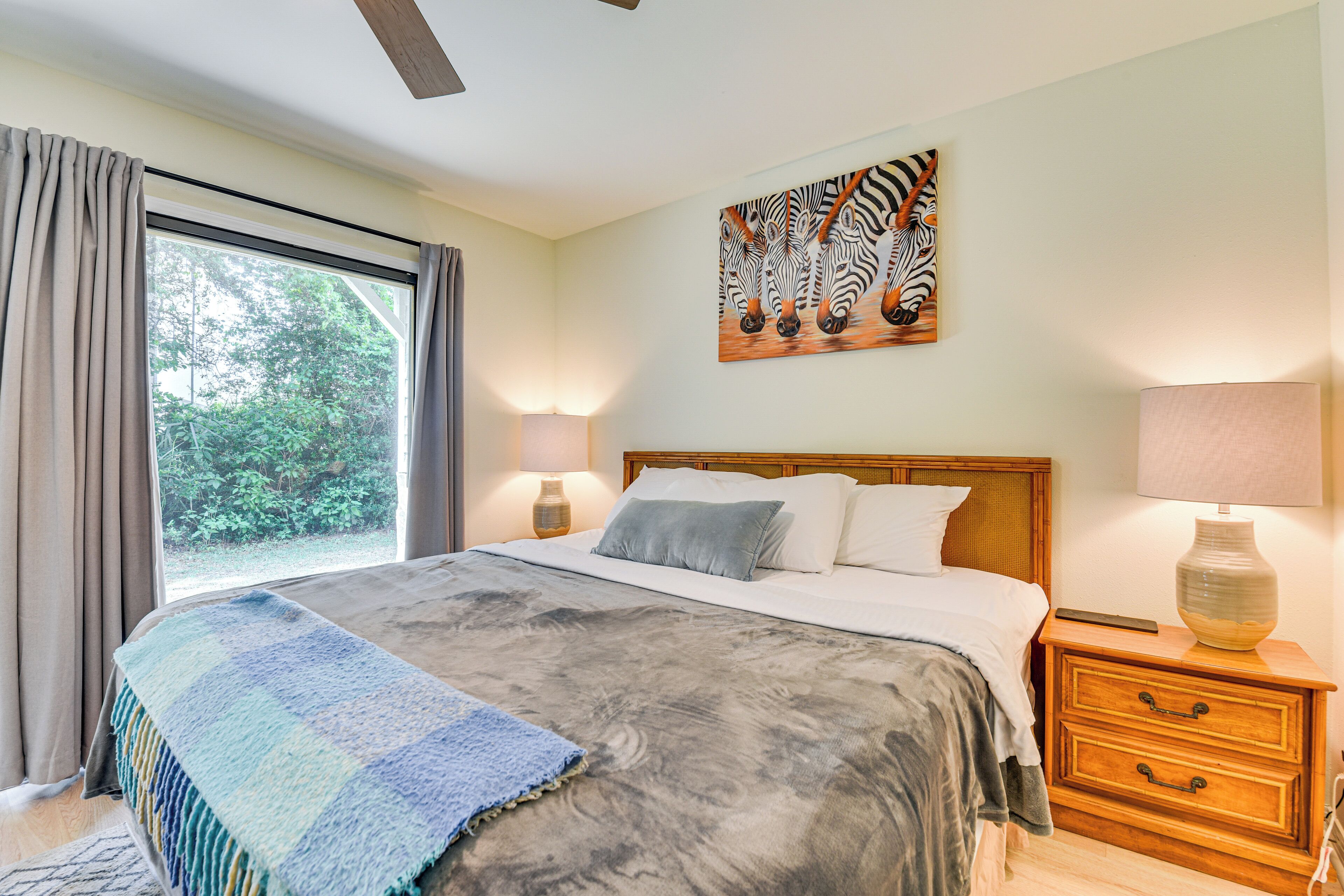 Une chambre avec un grand lit, une table de chevet avec une lampe, un tableau représentant des zèbres accroché au mur et une vue sur la verdure à l’extérieur.