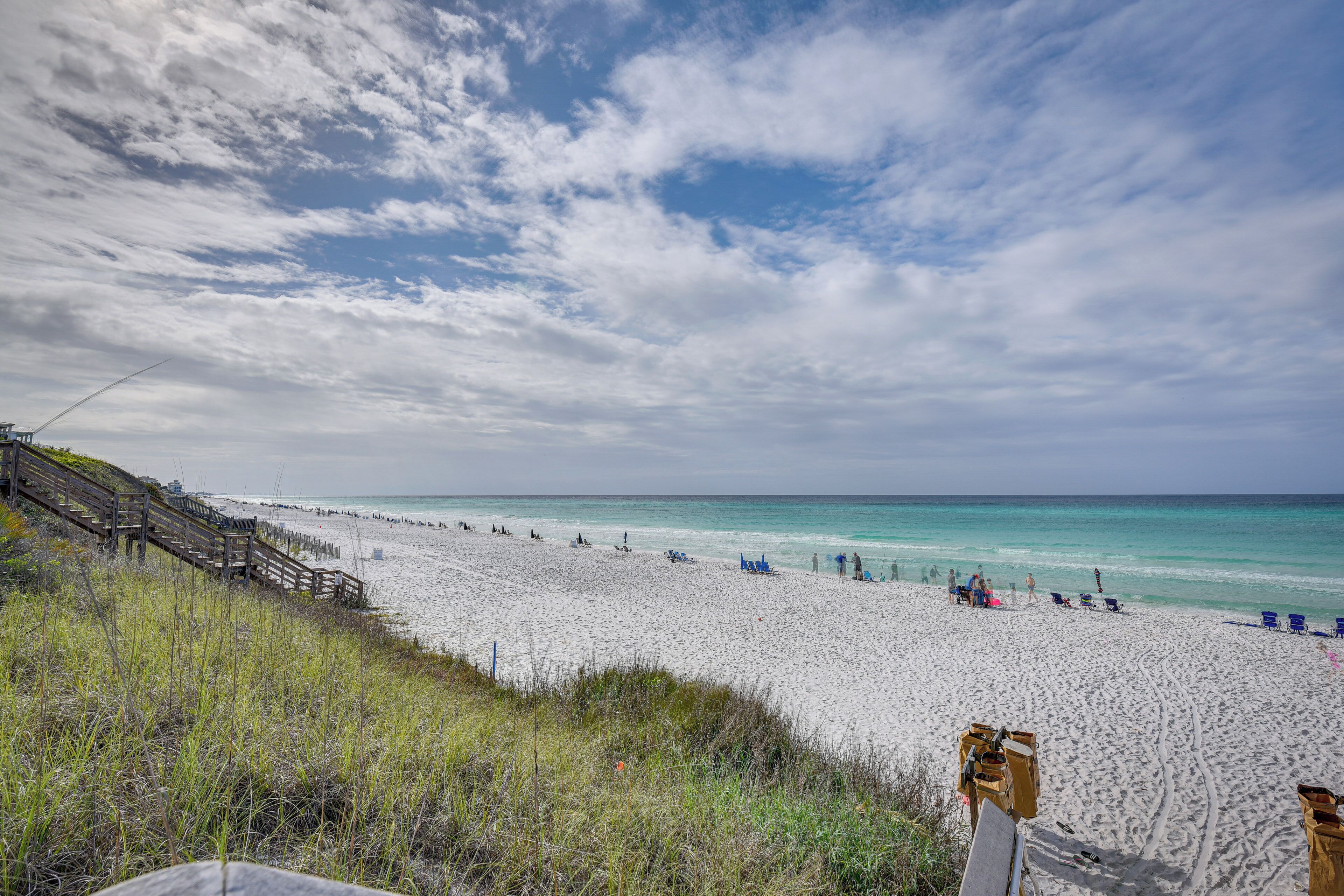 A beach with a wooden staircase leading down to the shore, a sandy beach, and a clear sky.