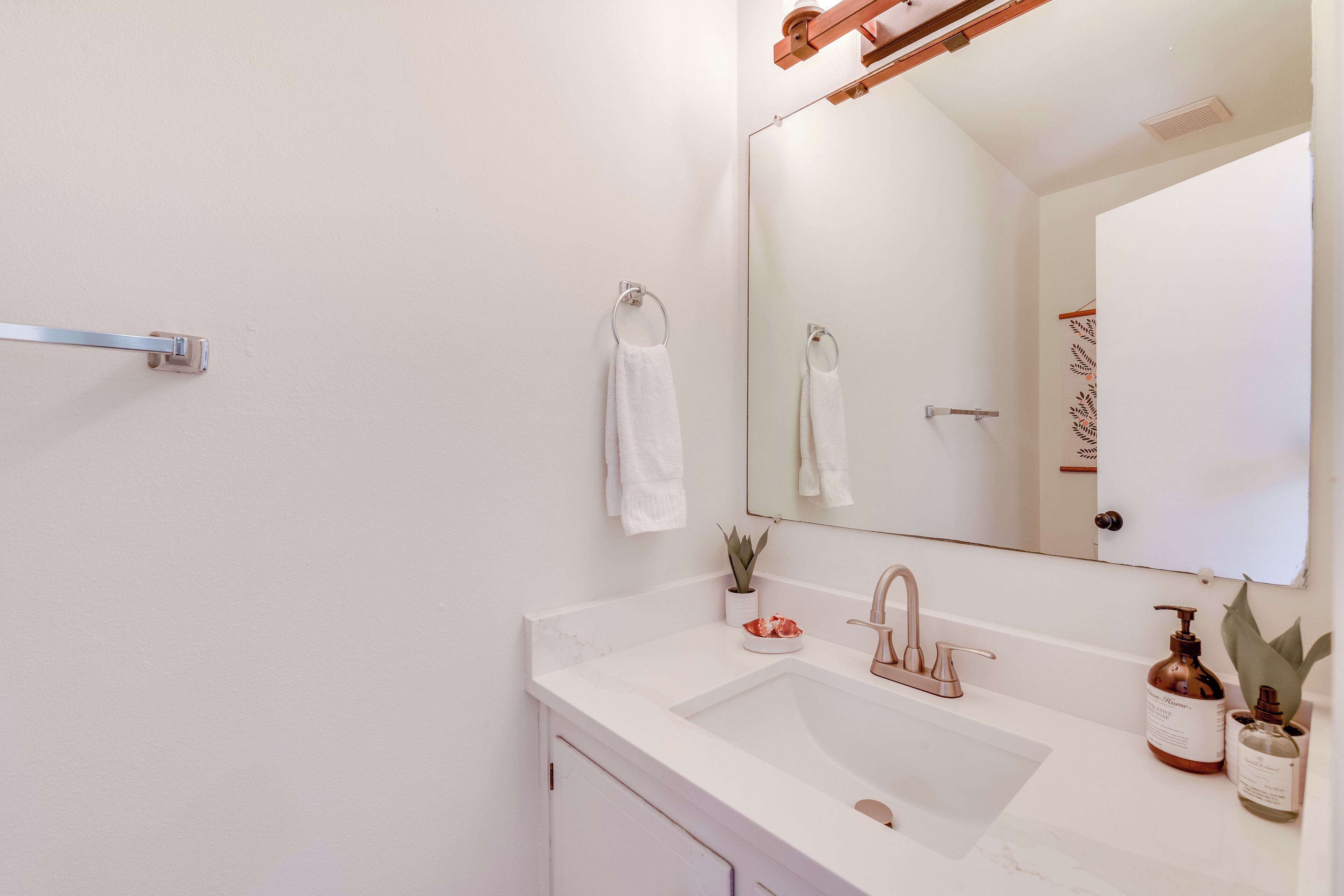 A modern bathroom with a white sink, a large mirror, and a towel rack.