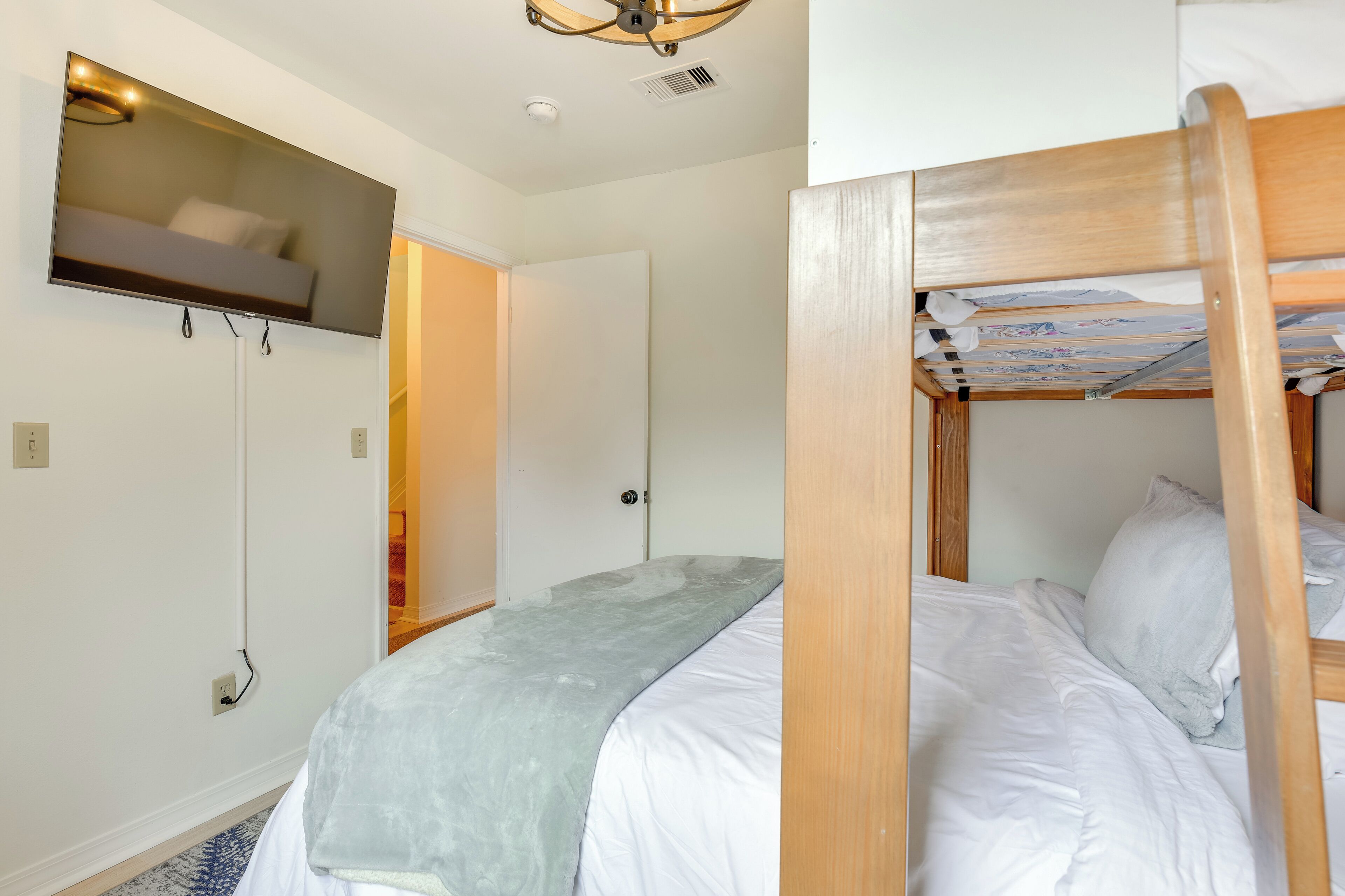 A bedroom with a bunk bed, a flat-screen TV mounted on the wall, and a ceiling fan.