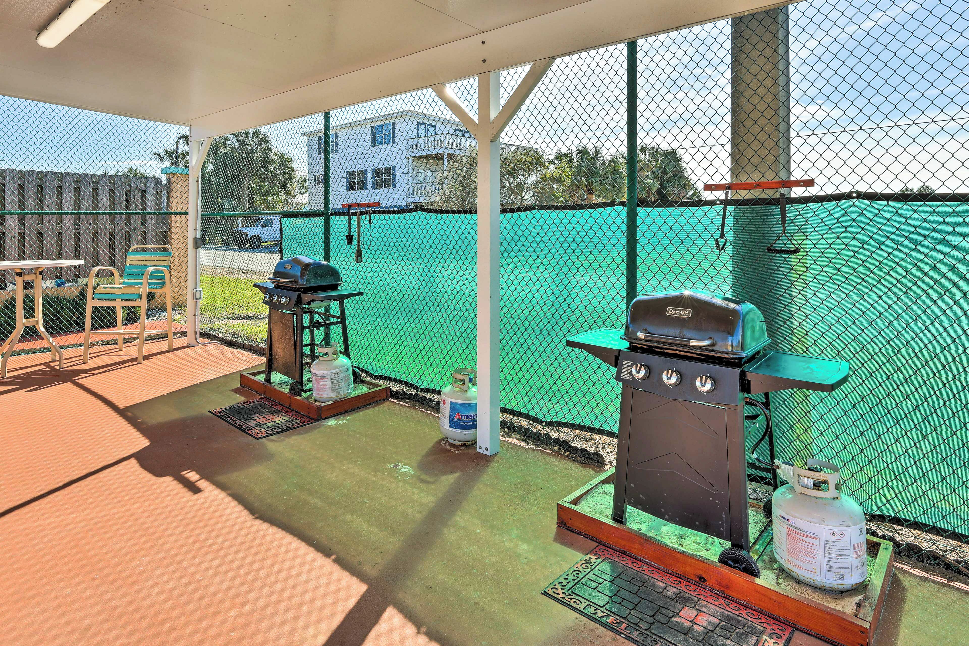 A covered outdoor area with a grill, seating, and a fenced tennis court.
