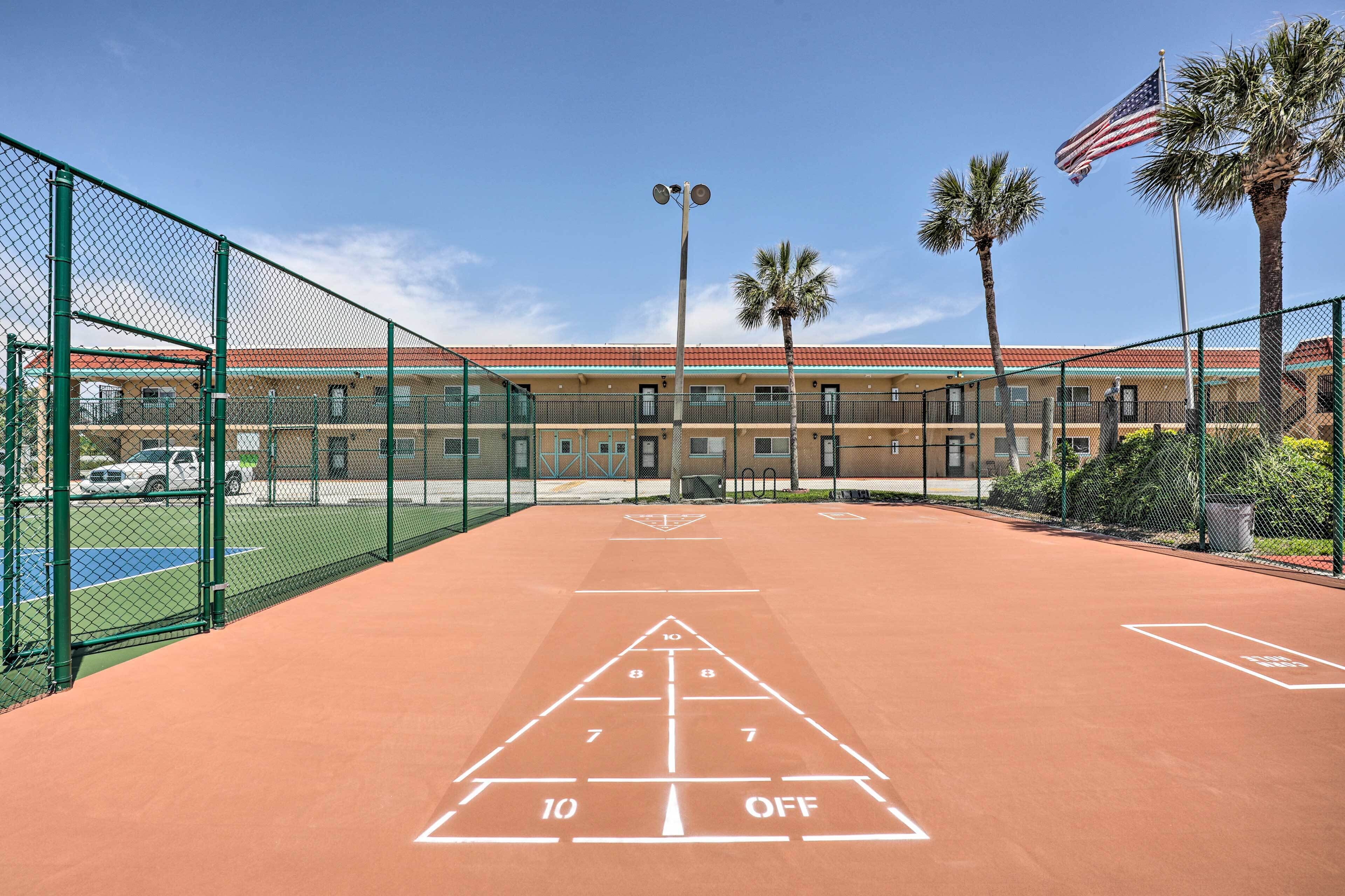 Un campo da shuffleboard con recinto a rete, un edificio con tetto rosso e palme.
