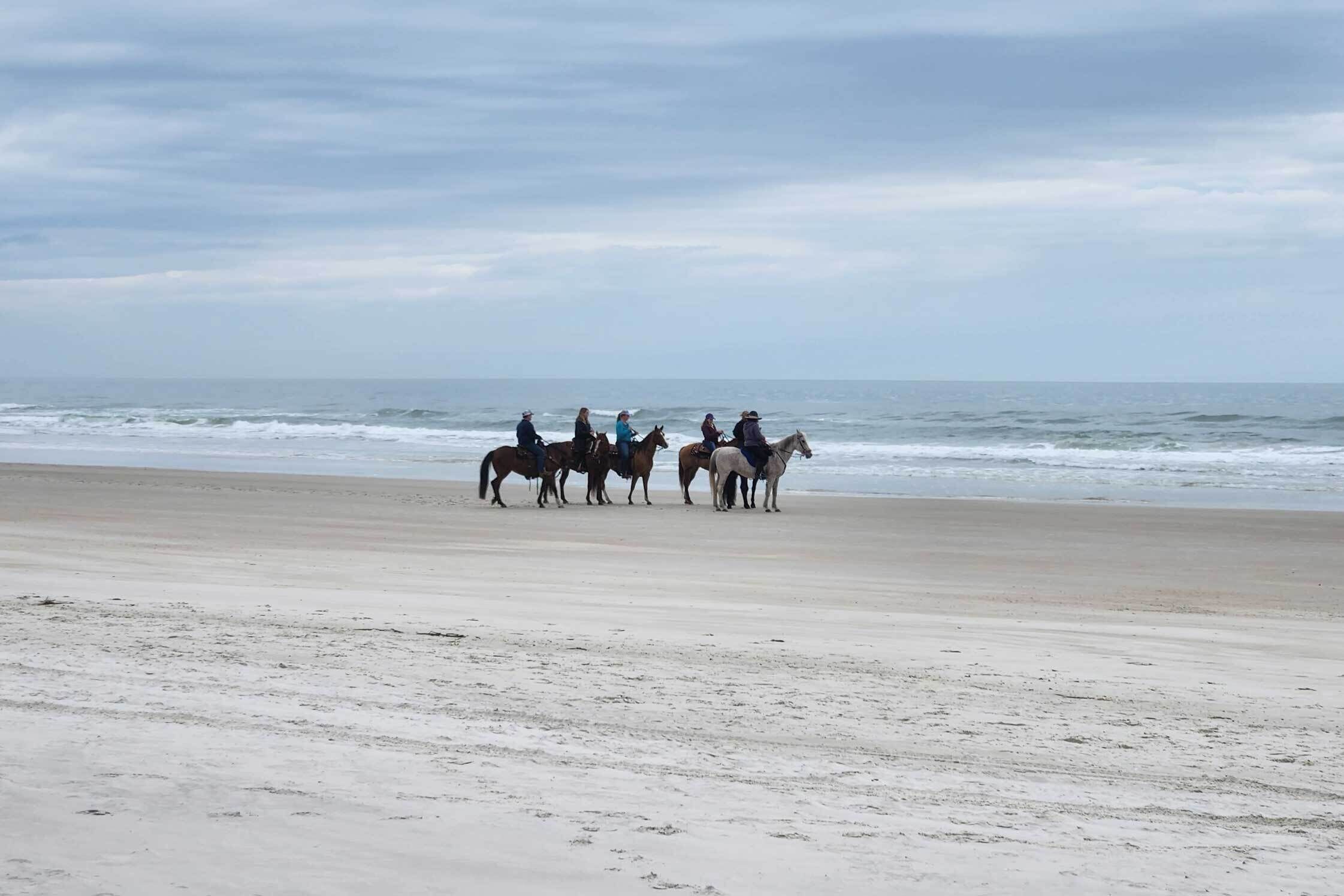 A beach with a group of horses and riders.