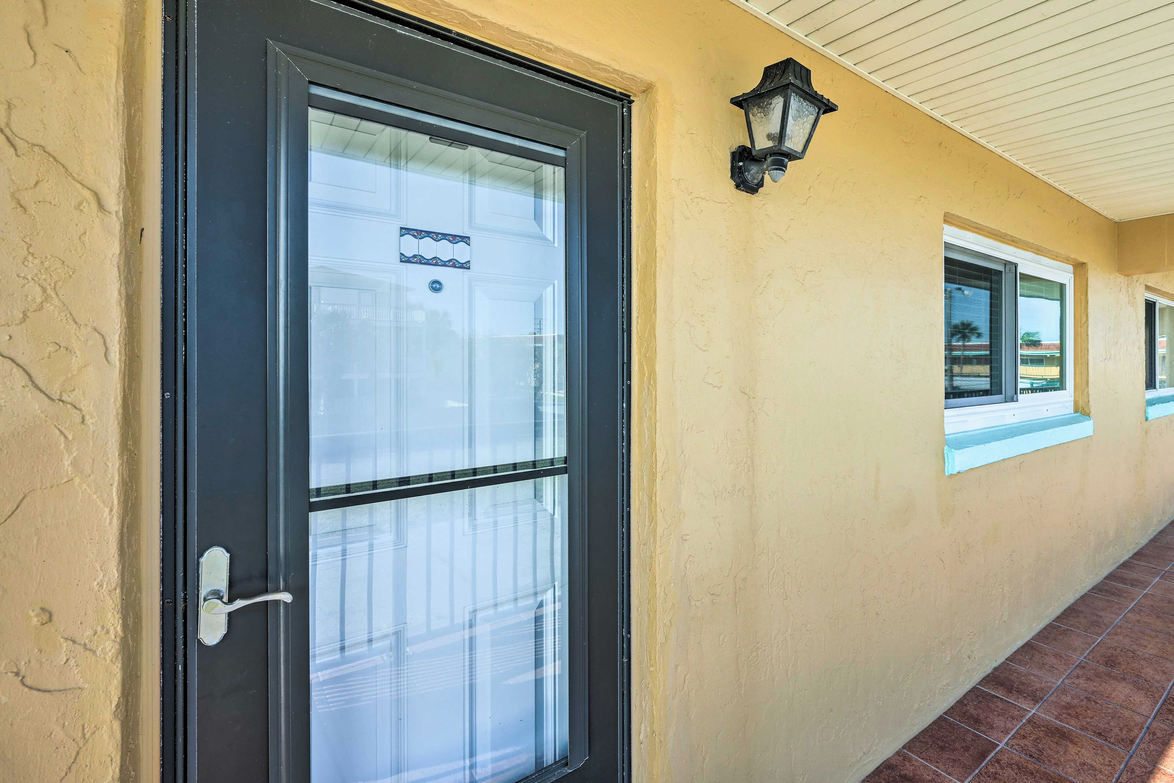 Um corredor com uma porta, uma janela e um luminário fixado na parede.