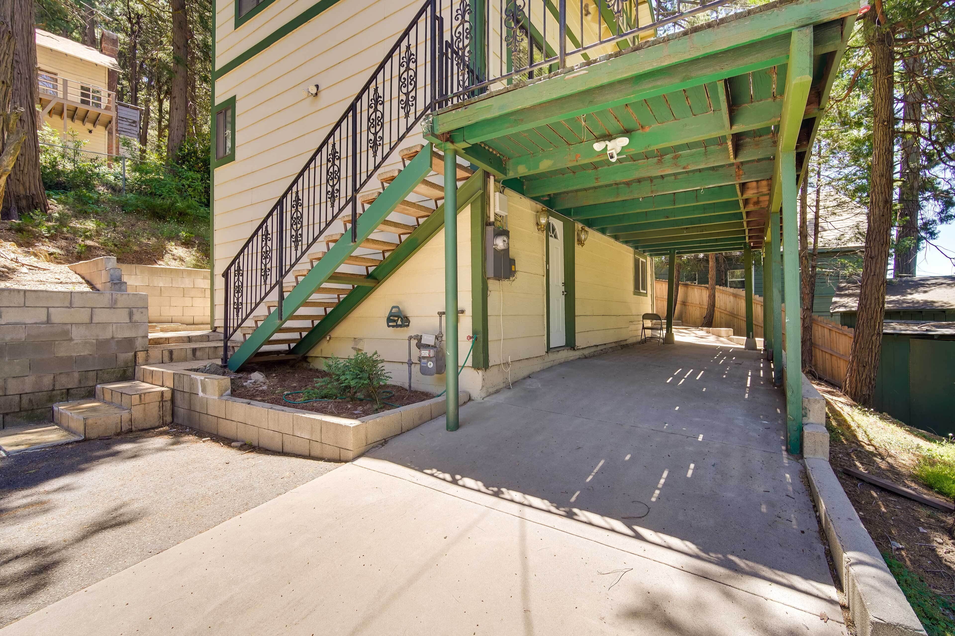 A covered outdoor area with a staircase leading to a building, surrounded by trees.