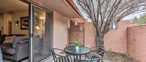 A patio with a round table and chairs, a potted plant, and a sliding glass door leading to a living room.