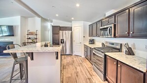 A modern kitchen with dark wood cabinets, a stainless steel refrigerator, a built-in oven, and a marble countertop island with bar stools.