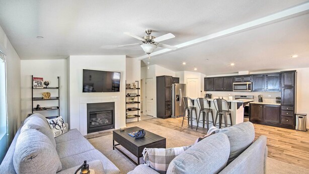 A modern living room with a fireplace, grey sofas, a coffee table, and a kitchen area with dark cabinets and a microwave.