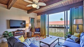 A living room with a television, sofa, armchair, and a balcony with a view.
