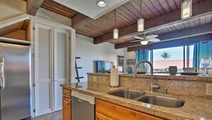 A kitchen with granite countertops, stainless steel appliances, wooden cabinets, and a ceiling fan.