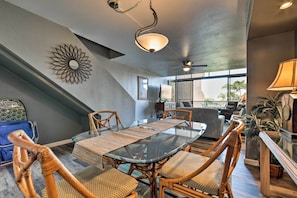 A dining area with a glass table, wicker chairs, a decorative wall piece, and a ceiling fan. - Resort Townhome w/ Pool - Walk to Pohaku Beach (Napili-Honokowai)