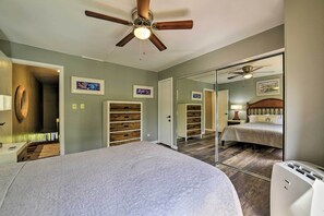 A bedroom with a large bed, a ceiling fan, a wardrobe, a mirror, and a door leading to another room. - Resort Townhome w/ Pool - Walk to Pohaku Beach (Napili-Honokowai)