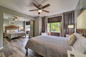 Habitación de hotel con una cama grande, ventilador de techo, ventana con cortinas y vista a zonas verdes.
