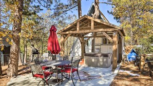 A covered outdoor dining area with a table and chairs, a hot tub, and a wooden pergola. - Cozy A-frame w/ Hot Tub Near Arrowbear Lake! (Running Springs)