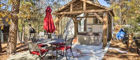 A covered outdoor dining area with a table and chairs, a hot tub, and a wooden pergola.
