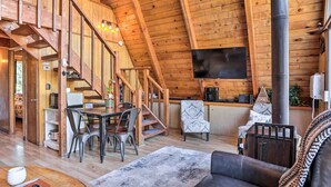 A wooden interior with a dining area, a sofa, and a TV mounted on the wall. - Cozy A-frame w/ Hot Tub Near Arrowbear Lake! (Running Springs)