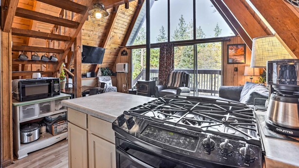 A rustic kitchen with a large stove, wooden beams, and a view of the outdoors. - Cozy A-frame w/ Hot Tub Near Arrowbear Lake! (Running Springs)