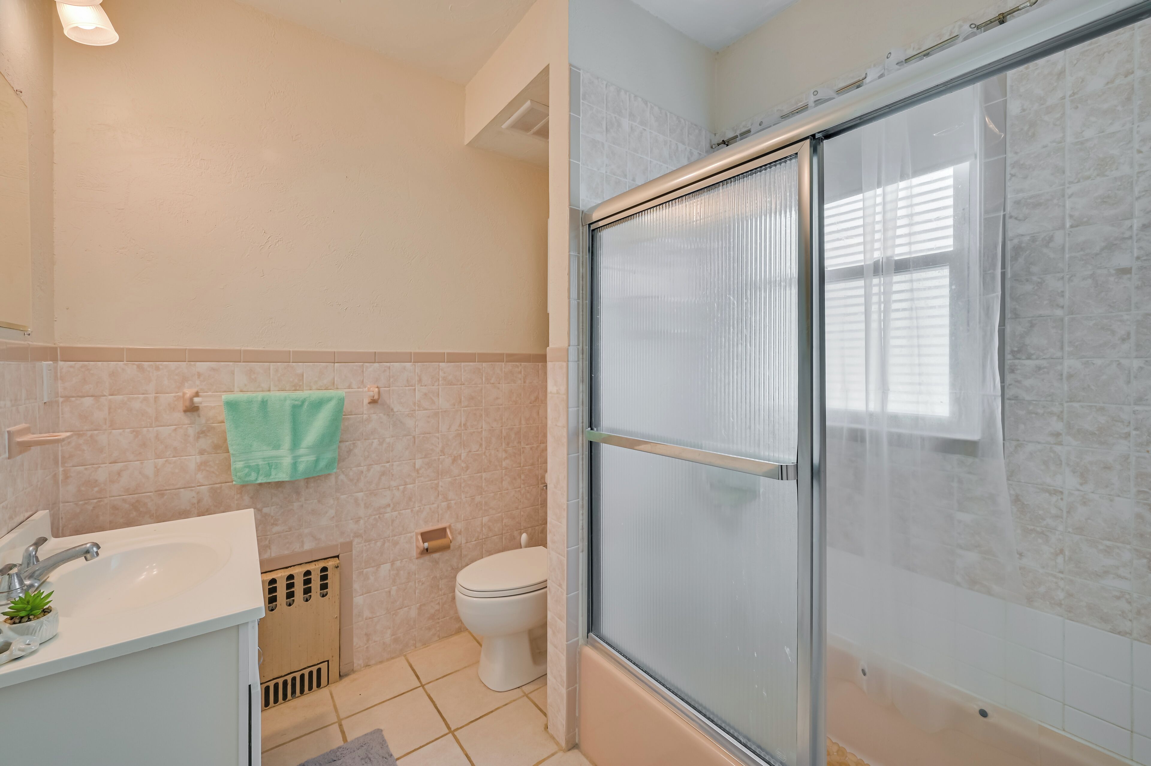 A bathroom with a shower, toilet, sink, and a towel hanging on the wall.