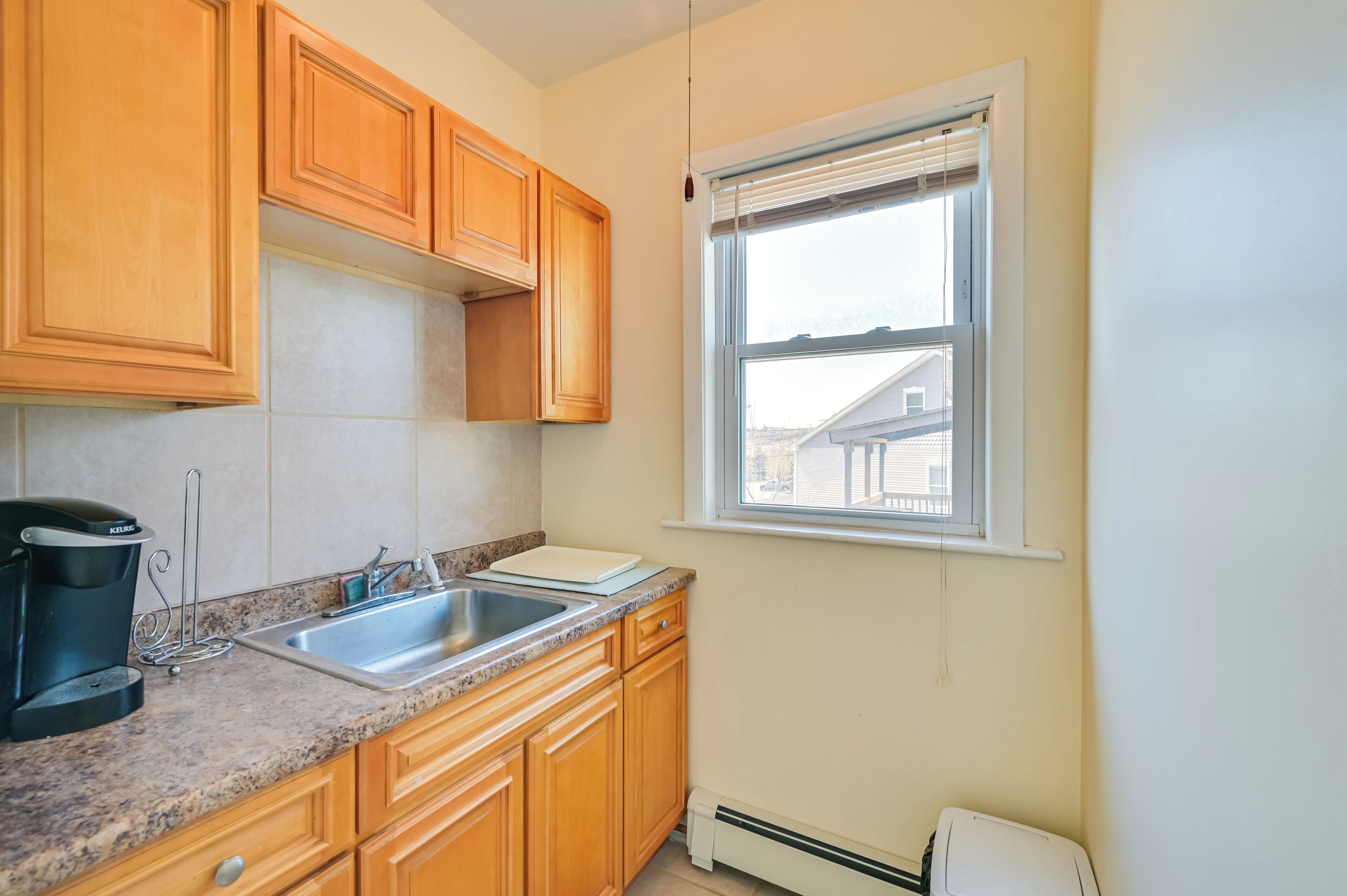 A kitchen with wooden cabinets, a granite countertop, a sink, and a window with blinds.