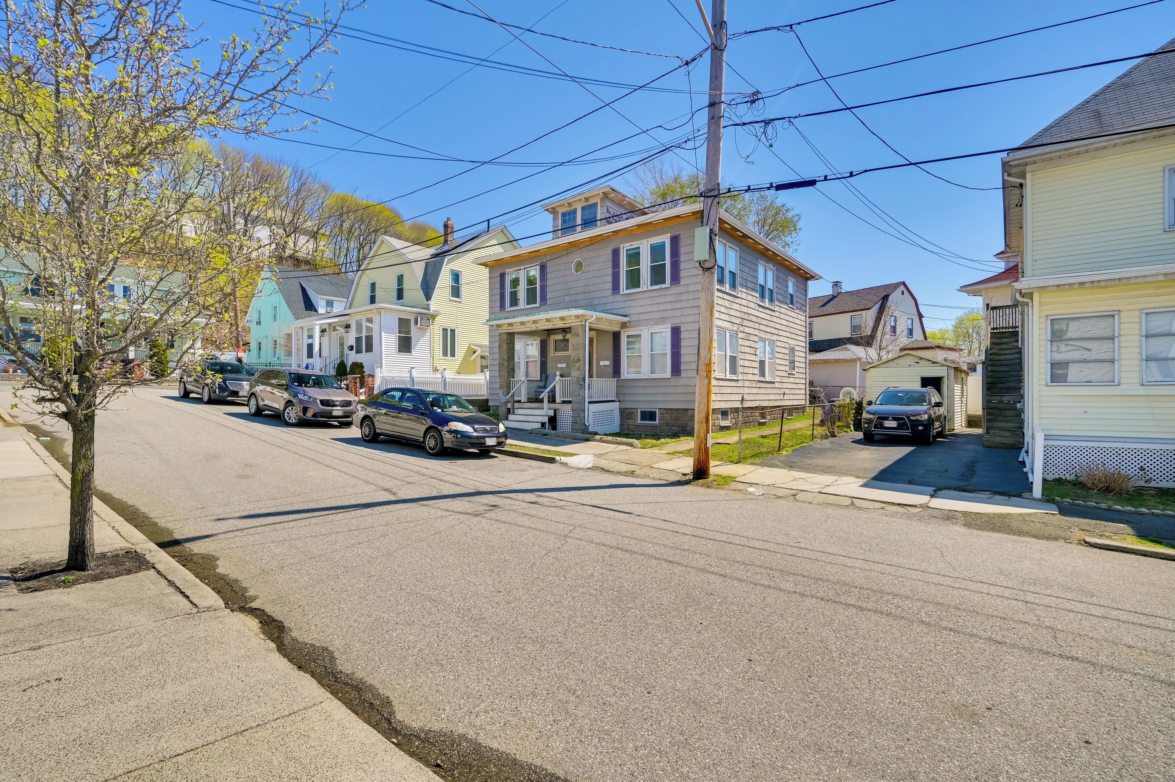 Une rue résidentielle bordée de maisons, de voitures garées et de poteaux électriques.