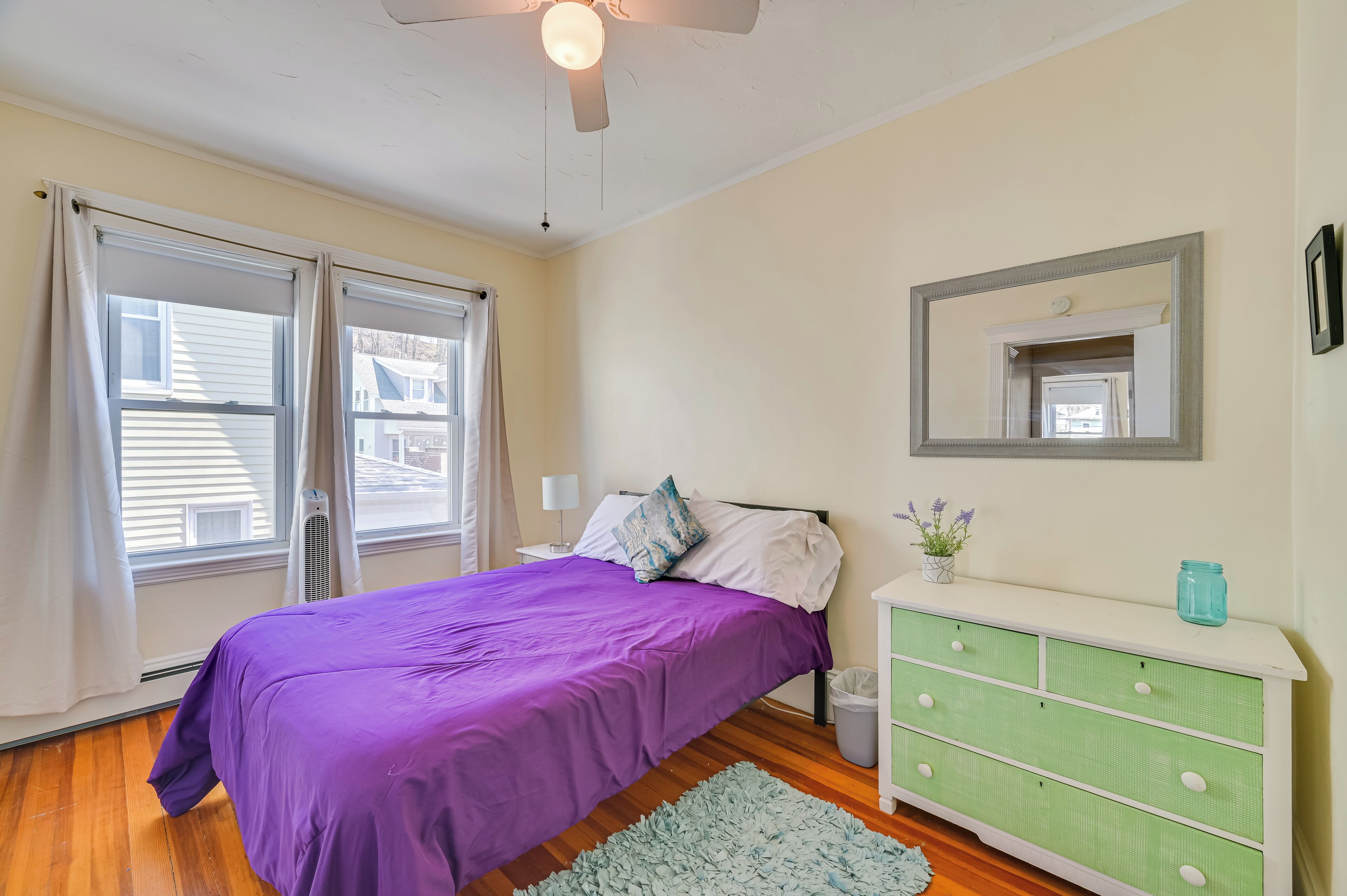 A bedroom with a bed, a dresser, a mirror, and a ceiling fan.
