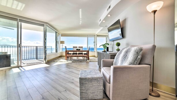 A spacious living area with a balcony, a sofa, a television, and a floor lamp.