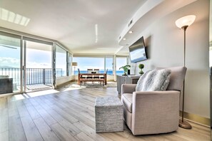 A spacious living area with a balcony, a sofa, a television, and a floor lamp. - Luxurious Maui Getaway w/ Panoramic Ocean Views! (Wailuku)
