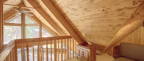 Un interior de madera con techo inclinado, un ventilador de techo y vistas a través de una ventana.