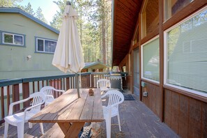 Une terrasse en bois avec une table de pique-nique et des chaises, un barbecue et un parasol.