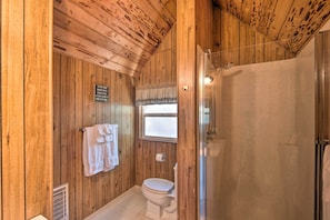 A wooden-paneled bathroom with a toilet, a shower, and a window.