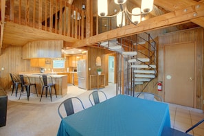 Une cuisine spacieuse dotée de meubles en bois et d’un îlot central, un coin repas avec une table et des chaises, et un escalier en colimaçon menant à un niveau supérieur.