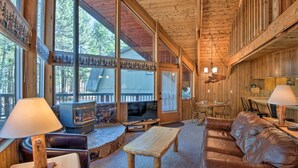 A cozy cabin interior with a fireplace, leather sofa, wooden tables, and large windows offering a view of the forest. - 5 Mi to Heavenly Mountain Resort: All-seasons Gem (South Lake Tahoe)