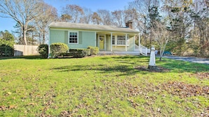 A single-story house with a front porch, a small front yard, and a wooden fence. - Hen Cove Home w/ Wood Deck - Walk to Beaches! (Cataumet)