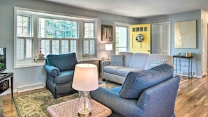 A living room with two sofas, a lamp, and a decorative wall piece. - Hen Cove Home w/ Wood Deck - Walk to Beaches! (Cataumet)