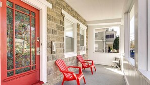 Un edificio con puerta roja, dos sillas Adirondack rojas y un muro de piedra.