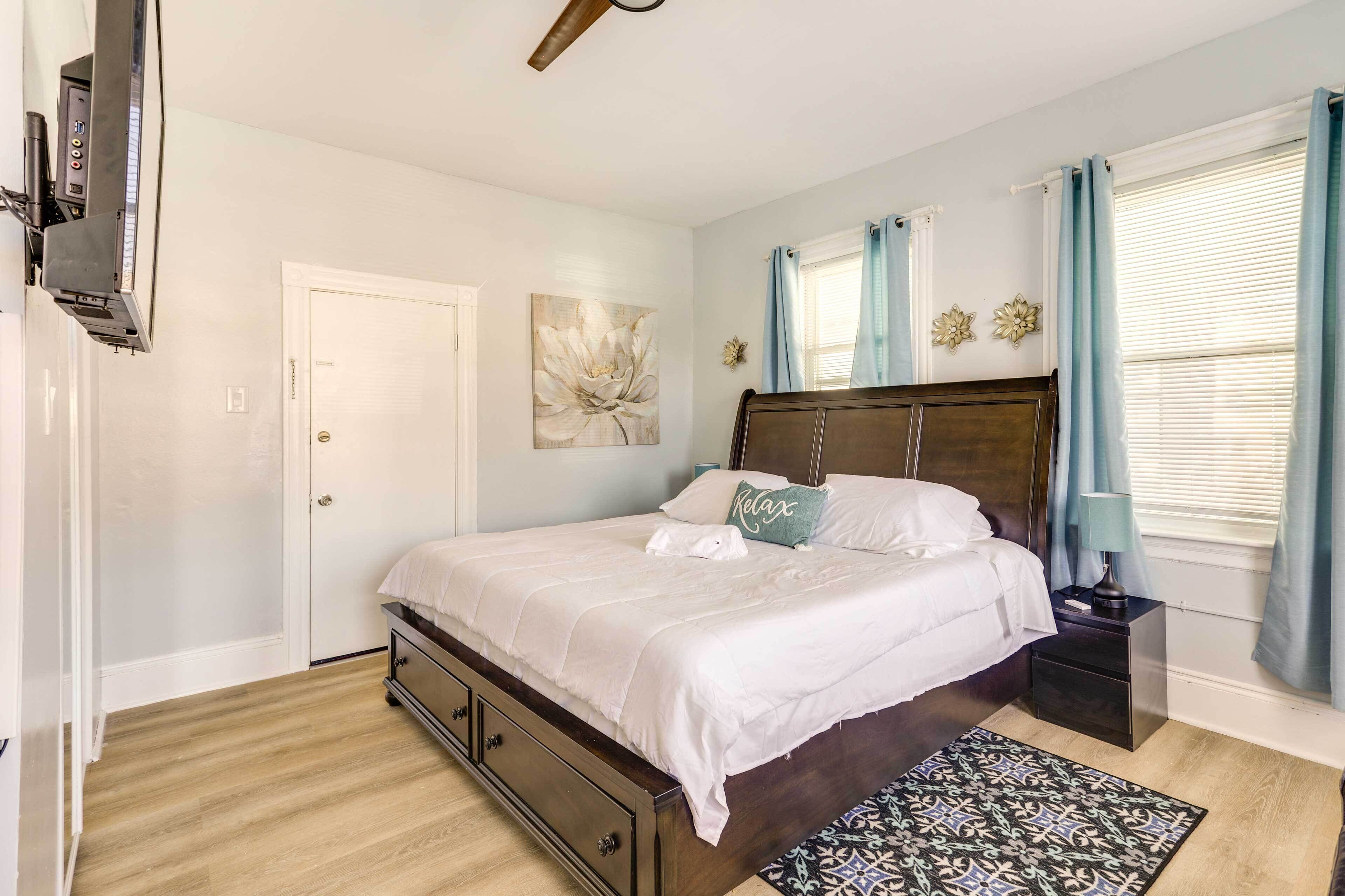 A bedroom with a large bed, a nightstand, a wall-mounted TV, and a window with curtains.