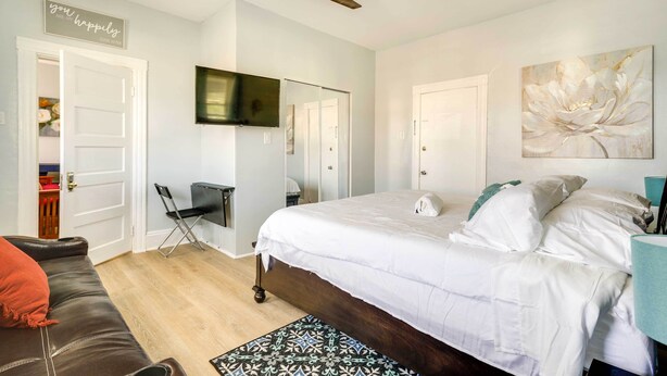 Un dormitorio con una cama, un ventilador de techo, un televisor y un cuadro grande con motivos florales.